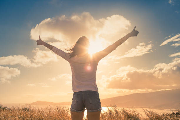 Person in a field at sunset, arms raised in triumph, silhouetted against glowing clouds and warm sky.