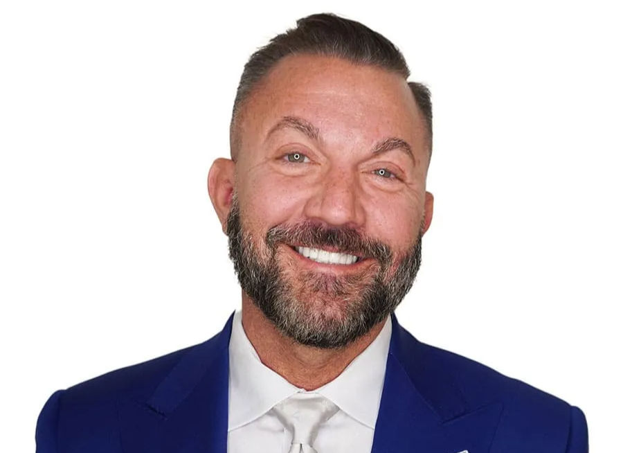 Smiling man with a beard in a blue suit and white shirt against a plain white background.
