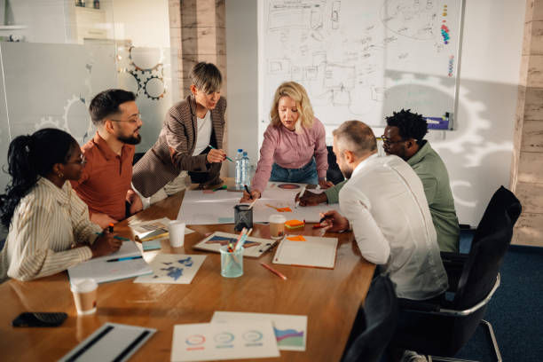 Smiling diverse group in a bright meeting room, seated in a circle and discussing with notebooks and papers in hand