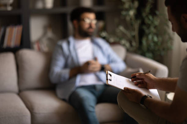 Therapist taking notes while a man sits on a couch in a cozy living room, suggesting a calm counseling session