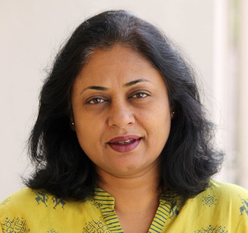 Portrait of a woman with shoulder-length black hair in a yellow patterned top, looking at camera against a plain light background.