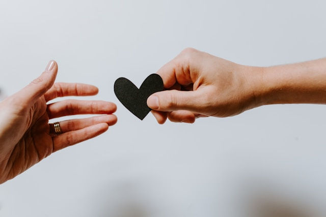 Person reaching black heart cut out paper