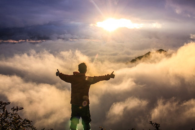 a man doing thumbs up with the clouds and under the sun