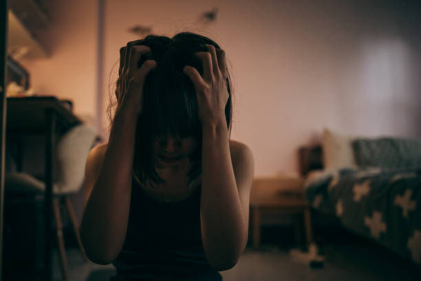 A depressed woman clutching her forehead in a dimly lit bedroom