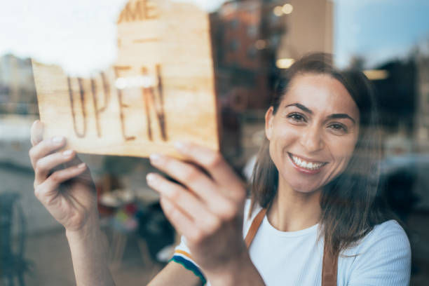Portrait of a happy business owner hanging an open sign on the door at a cafe and smiling.