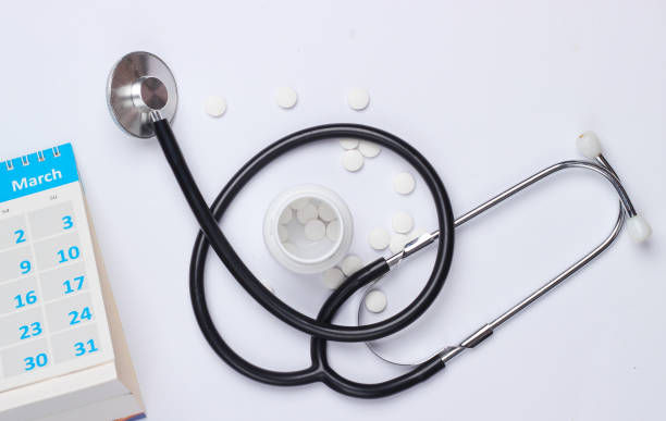 Bottle pills and stethoscope with desktop calendar on white background.
