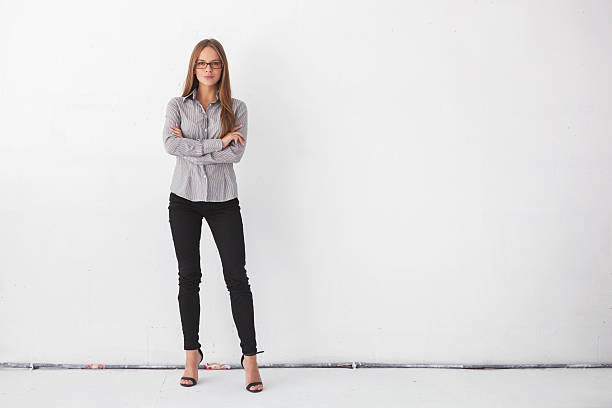 Portrait of young beautiful business woman standing against white wall.