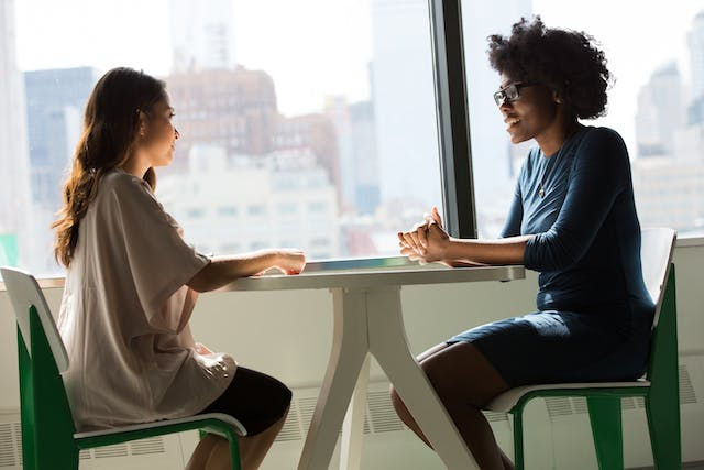 Two women sitting on chairs beside window