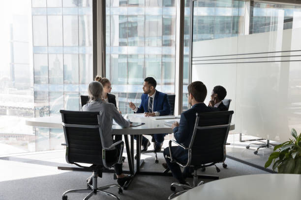 Serious team of professionals, five multi ethnic business people negotiating in modern boardroom.