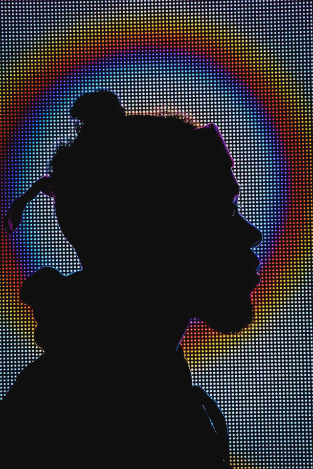 A man stands in the background, illuminated by various hues of light.