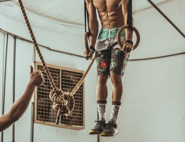 Man wearing multicolored shorts while exercising on rope inside white room.