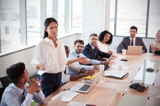 Businesswoman stands to address meeting around board table