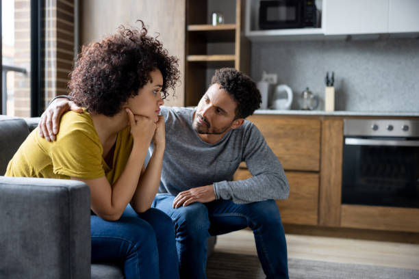 A photo of a man comforting his girlfriend at home while she is looking upset.