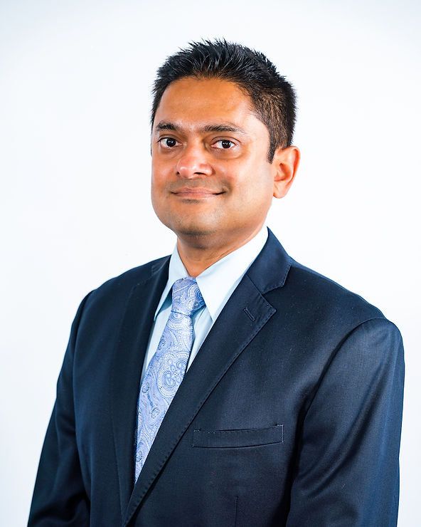 Man in a suit with a patterned tie smiles against a plain white background, conveying a professional and confident mood.