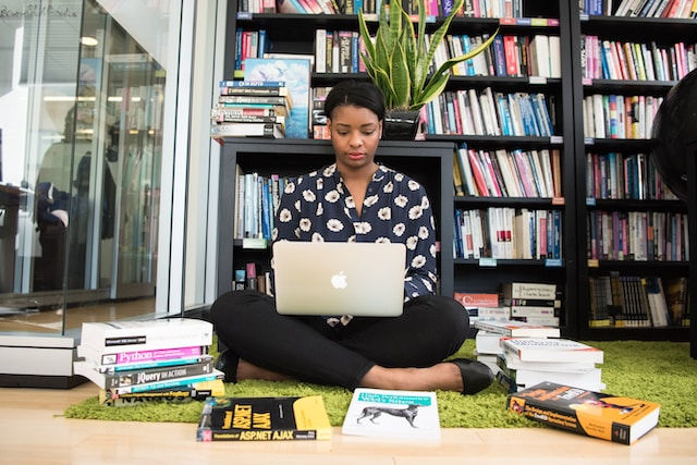 Woman sitting down surrounded by books while using laptop