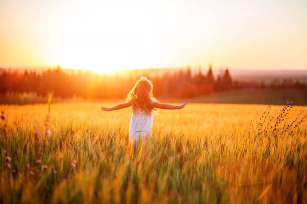 A photo of a little girl in white dress in field at sunset.