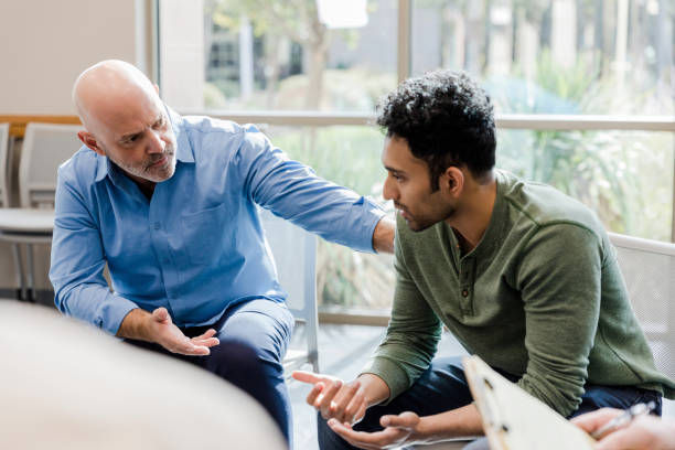 mature adult man gestures and asks questions as he helps the younger man work through his problems