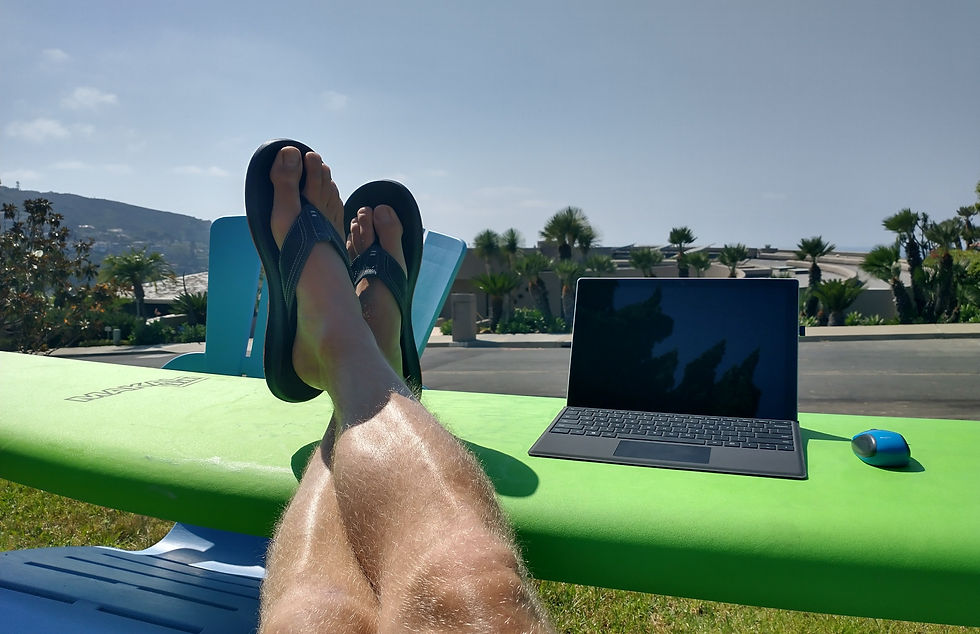 A laptop and feet of a man resting on a green table relaxing outside the house
