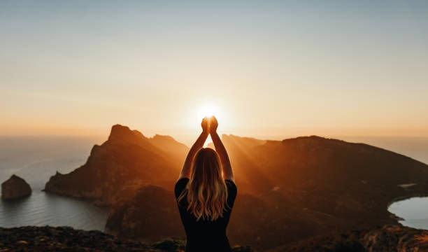Young woman in spiritual pose holding the light in front of mountains.