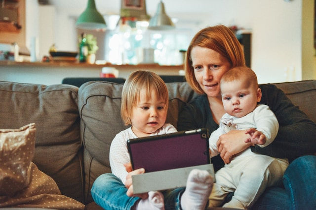 two babies and woman sitting on sofa watching on tablet