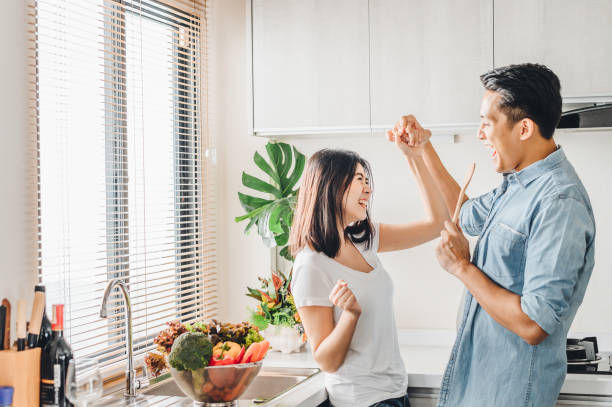 Romantic couple in love is dancing and smiling while cooking together in kitchen.