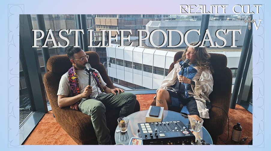 Two people sit in armchairs recording the "Past Life Podcast." Each has a microphone. They're in front of large windows with city views.