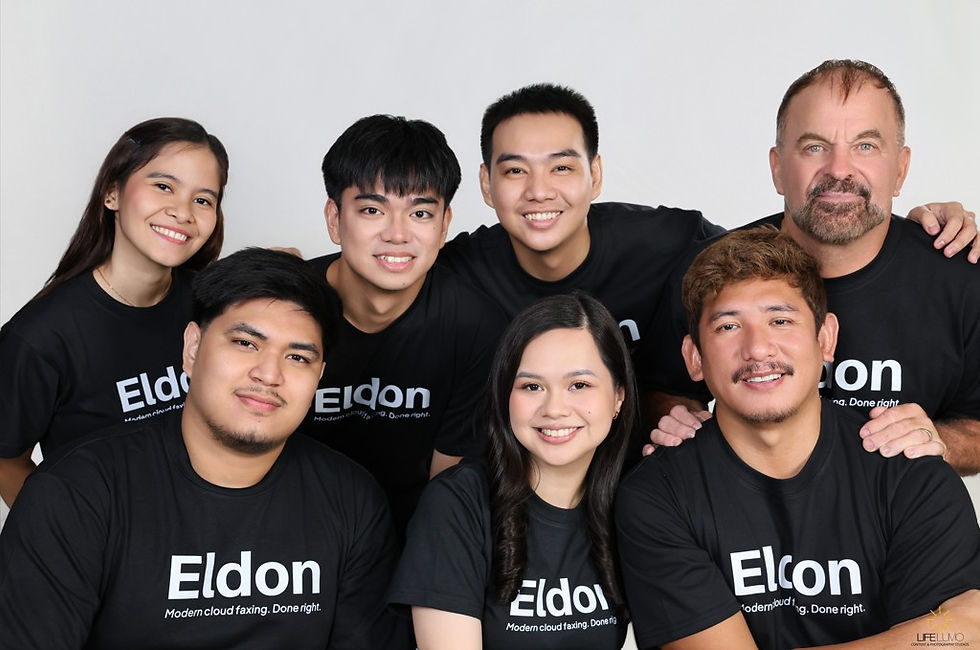 Smiling team in black Eldon T-shirts poses together against a plain light backdrop in a studio-style group portrait.