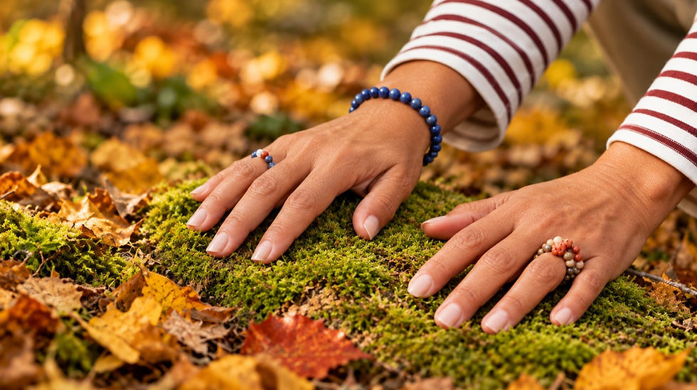 Close-up of hands with beaded bracelets resting on moss among autumn leaves, wearing striped sleeves, in a calm outdoor scene.