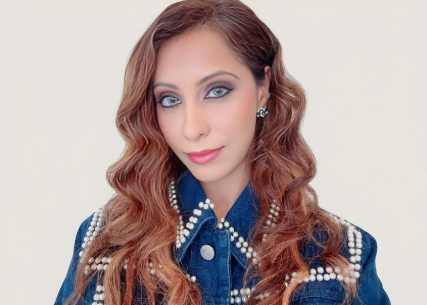 Portrait of a woman with wavy auburn hair and blue eyes wearing a pearl-trimmed denim jacket against a plain light background