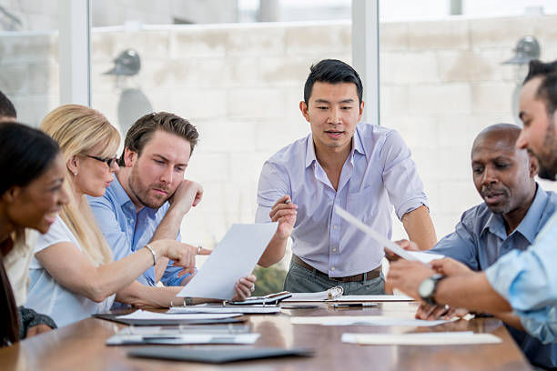 An associate is giving a presentation in the boardroom to a multi-ethnic group of business professionals.