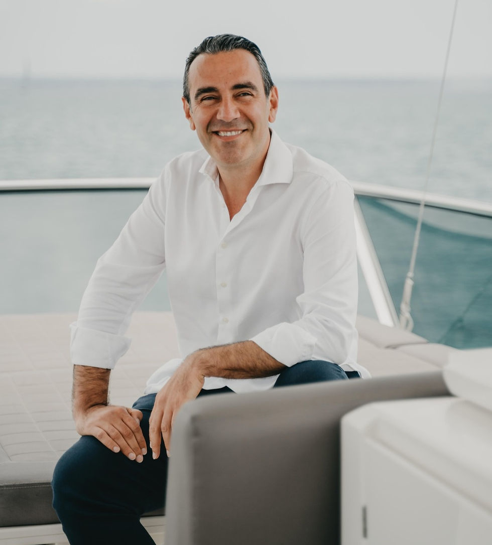 Smiling man in white shirt sits on a yacht, with a serene ocean background. The mood is relaxed and joyful. No visible text.