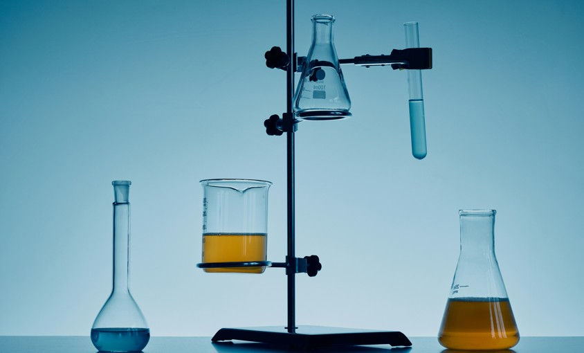 Laboratory glassware on a stand with blue and amber liquids in flasks and beakers against a cool blue background.