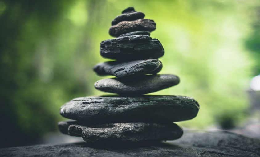 Stack of dark stones balanced on a rock, with a blurred green forest background and calm, zen-like mood