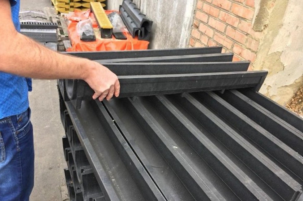 Man in blue shirt lifts a black slatted panel stack beside a brick wall at a construction site.