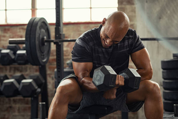 Muscular guy in sportswear lifting dumbbell while sitting on bench at cross training gym.
