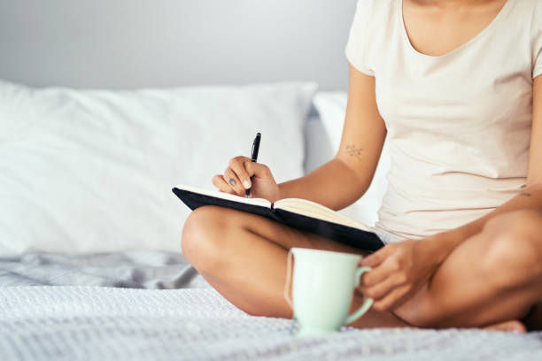 Cropped shot of a woman sitting on her bed and writing.