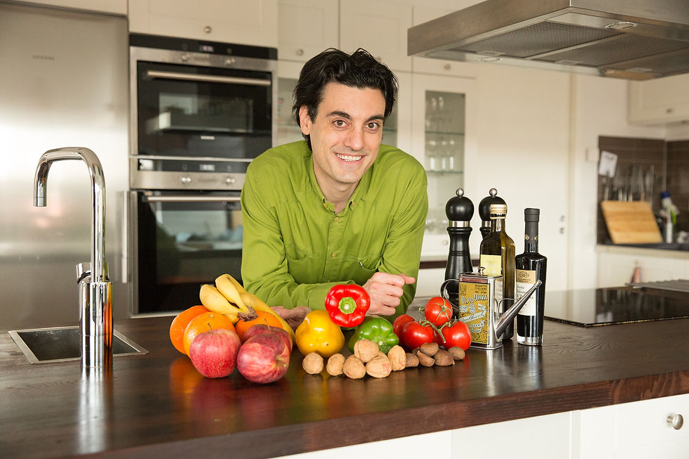 A guy standing near the kitchen sink with fruits and vegetables on his front.