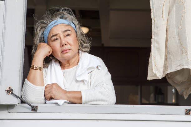 unhappy senior woman looking out of window alone at home