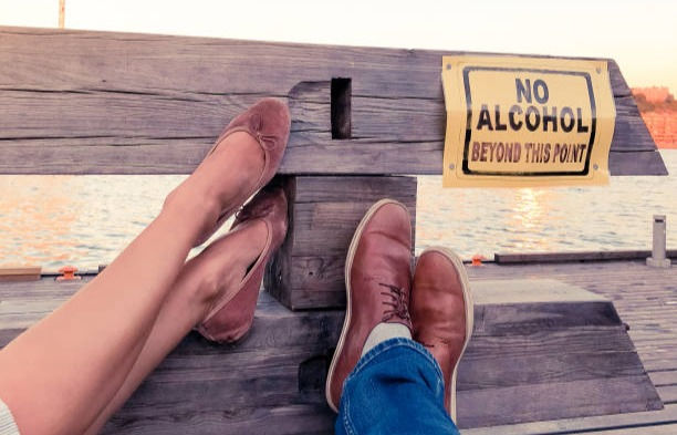 Legs of a man and a women pointing to a sign ''No Alcohol beyond this point''