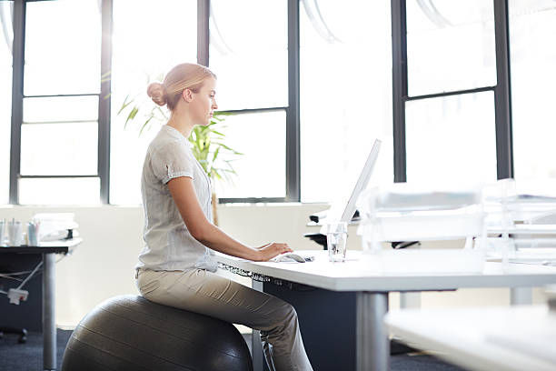 Shot of woman sitting on a swiss ball while working at her computer in an office. 