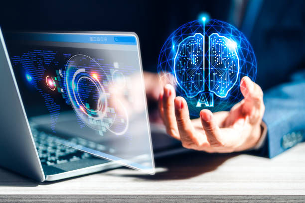   A man working on his computer while holding a 3D figure of a brain.
