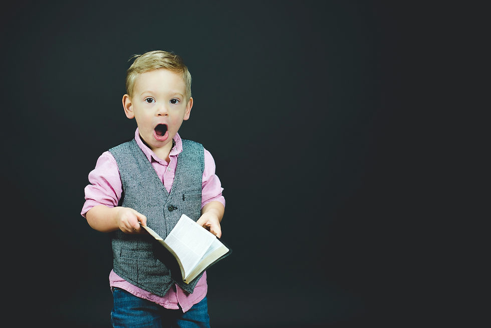 Boy wearing vest and pink dress shirt holding a book. 