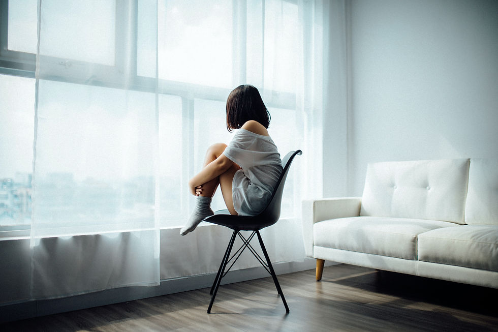A woman in white sitting comfortably on a chair overlooking at the window.