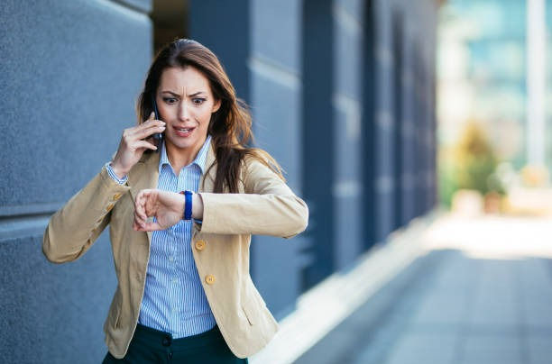 Businesswoman checking time on wristwatch while talking mobile phone outside..