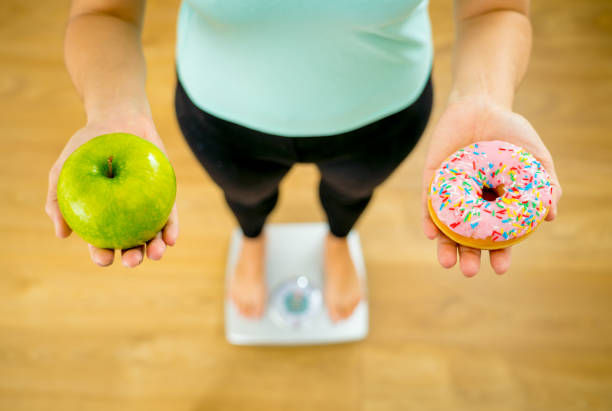 woman on scale holding on hands apple and doughnut.