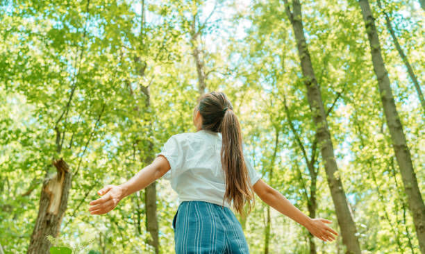 woman breathing clean air in nature forest with arms spread..
