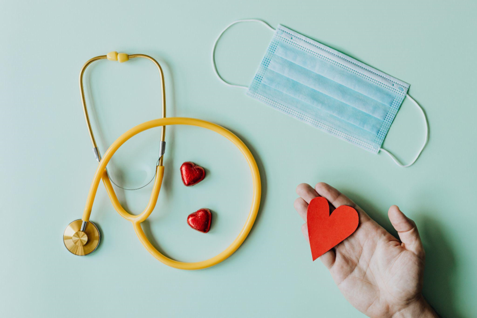 stethoscope, surgical mask and a hand holding a heart shape paper