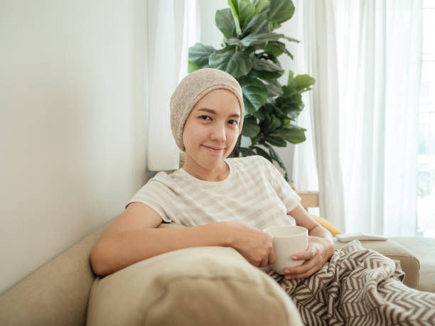 Female cancer patient wearing headscarf, she is looking happy. hopeful and sitting in the living room at her home.