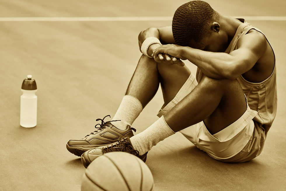 basketball player sitting on floor with his head down feeling tired.