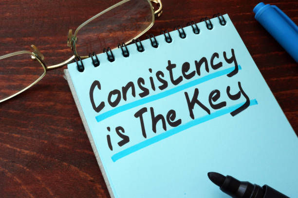 Consistency is The Key written on a notepad with marker and eye glass on the table.. 